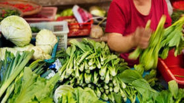 A person in a red shirt sorts and arranges green leafy vegetables at a market stall.