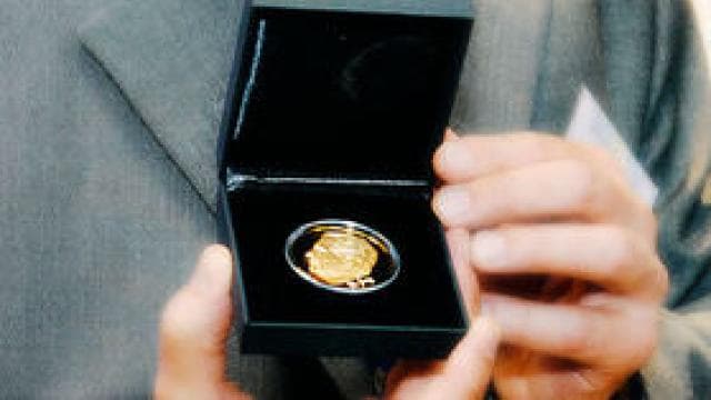 A person holds an open black box with a gold medal inside.