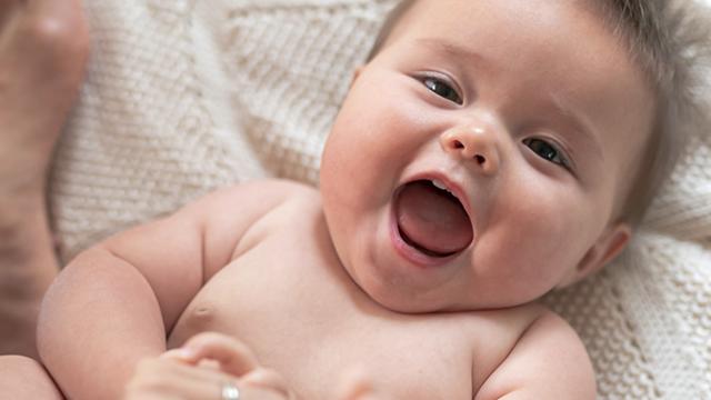 Um bebê deitado em um cobertor macio, sorrindo com a boca aberta.