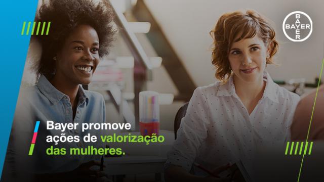 Duas mulheres sentadas juntas em uma mesa, sorrindo, com o logotipo da Bayer e o texto “Bayer promove ações de valorização das mulheres” na imagem.