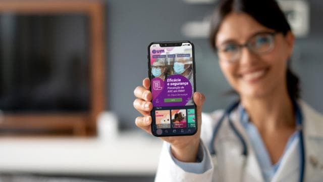 Uma pessoa vestindo um jaleco está segurando um smartphone exibindo uma interface de aplicativo relacionado à saúde.